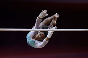 Gymnast Simone Biles twists through the air as she attempts to grab the uneven bars.